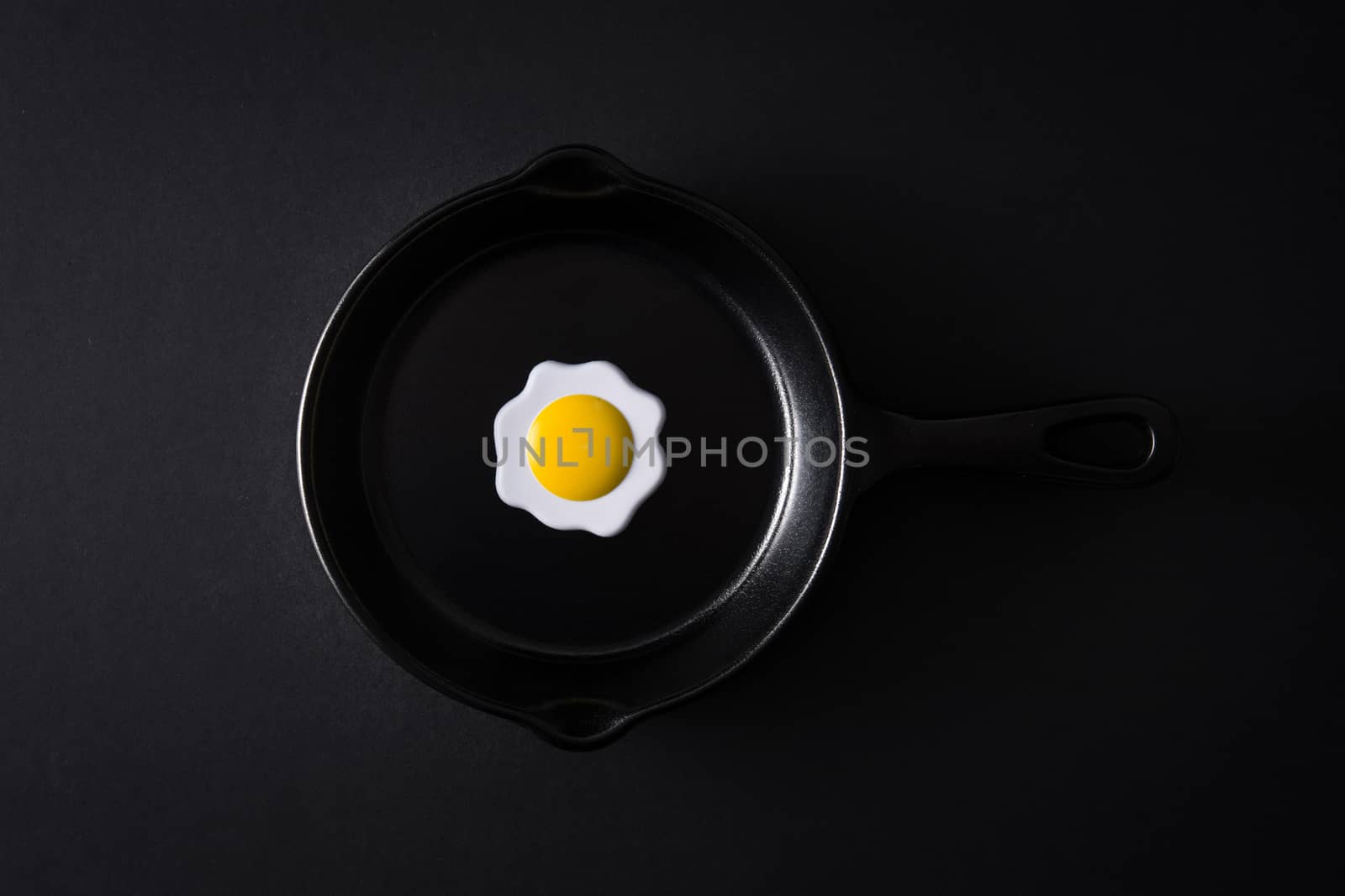 Black frying pan with egg inside on black background