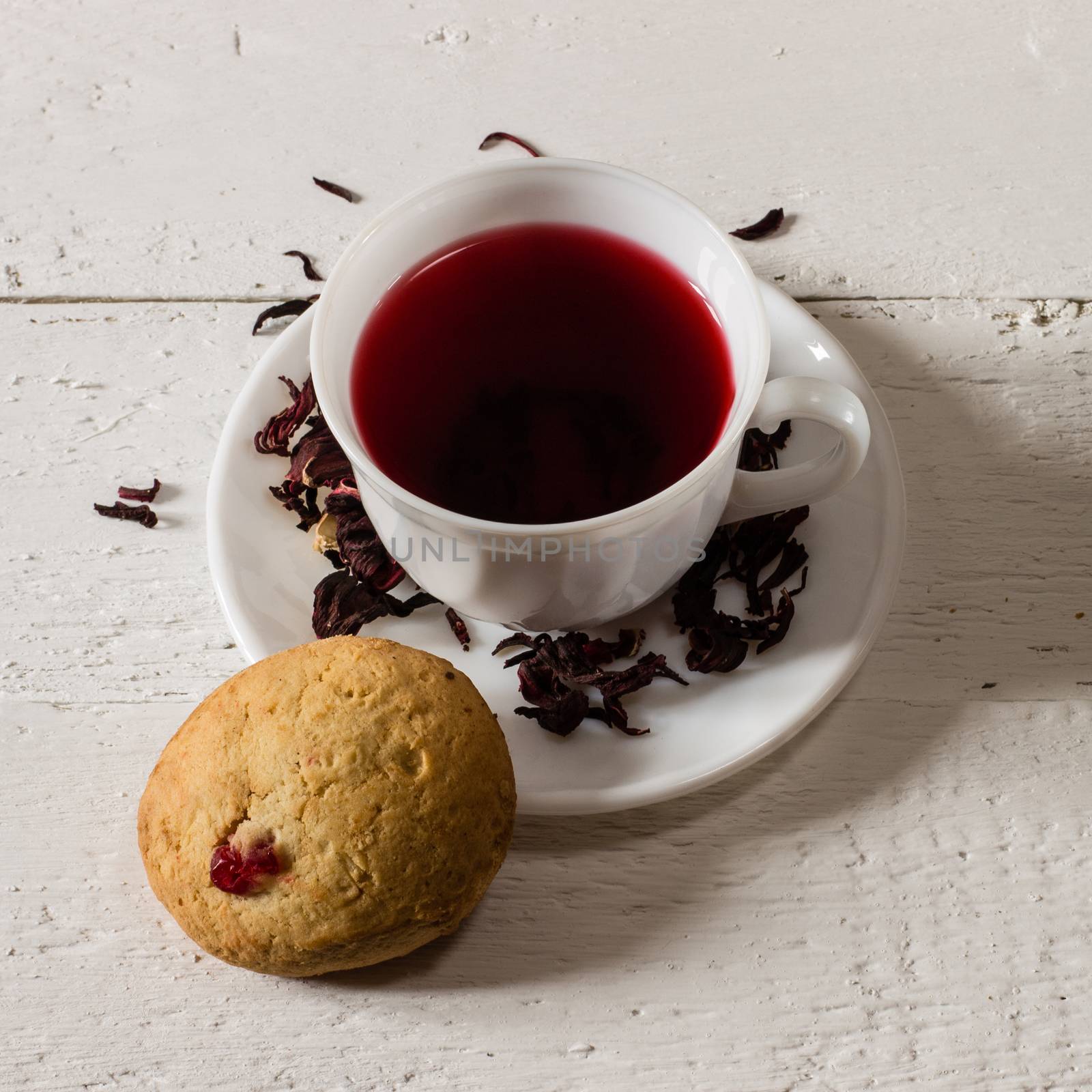 Cup of Karkadeh Red Tea with Dry Flowers and cookies on wooden table