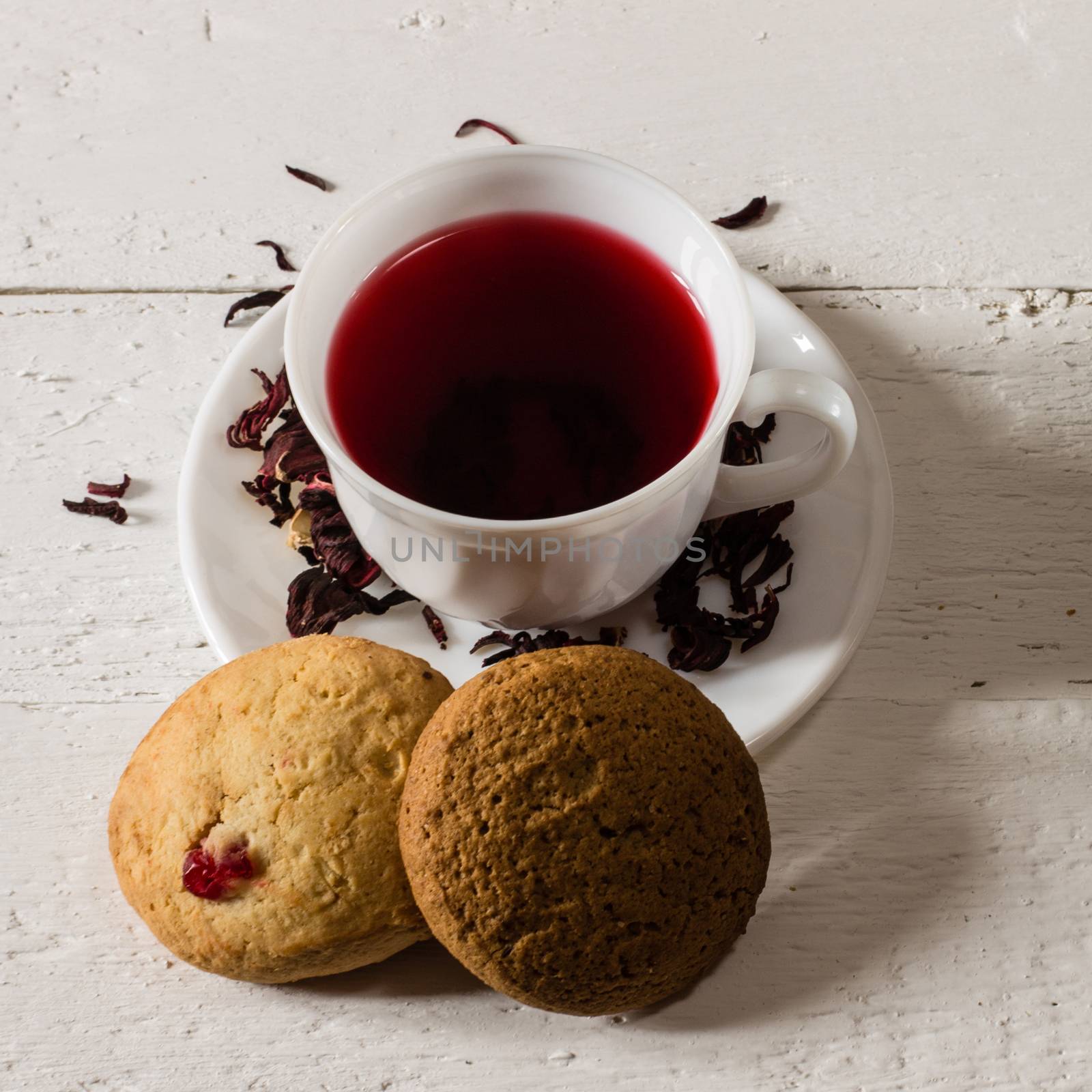 Cup of Karkadeh Red Tea with Dry Flowers and cookies on wooden table