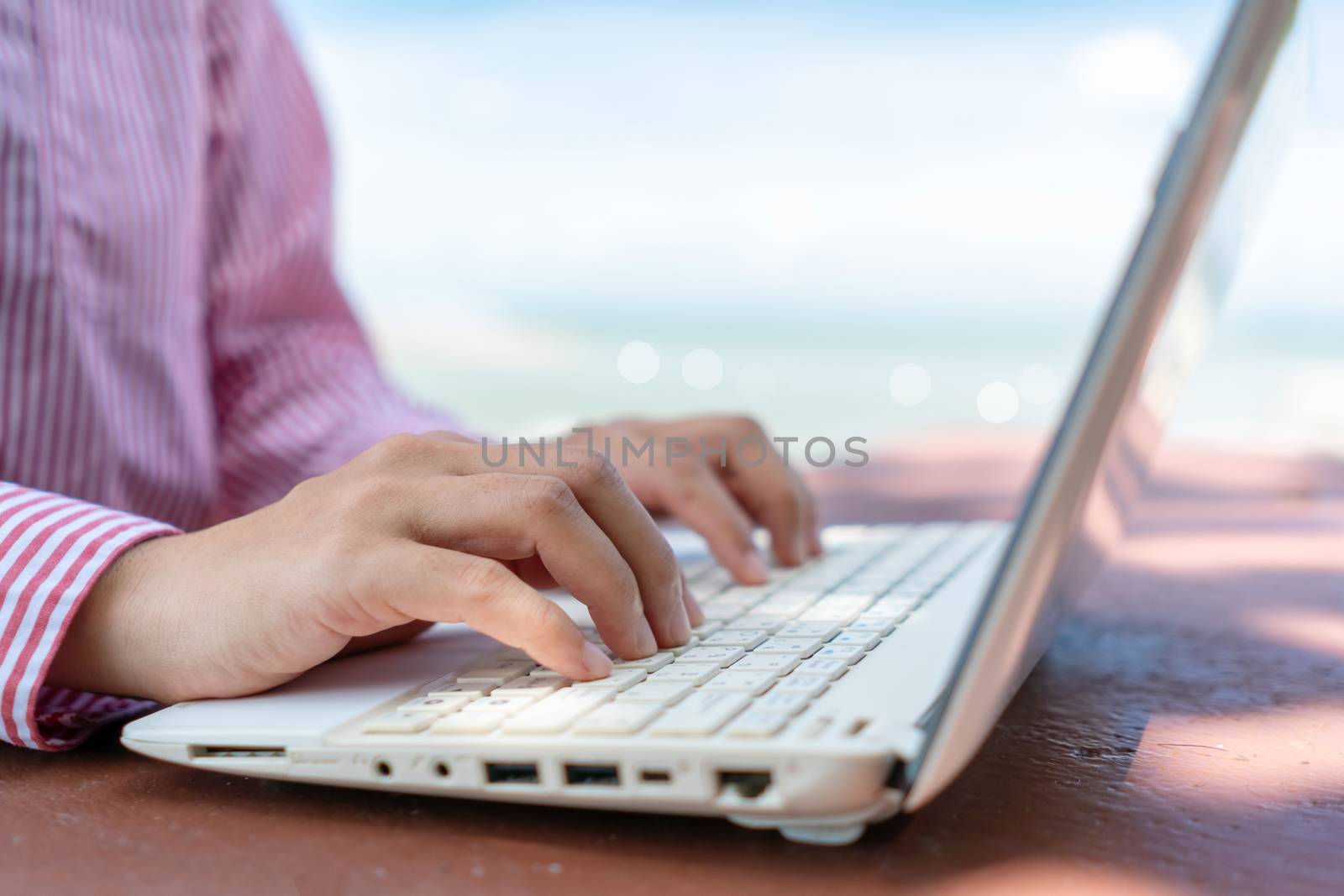 Woman hand using laptop to work study on work desk with clean nature beach outdoor background. Business, financial, trade stock maket and social network concept.