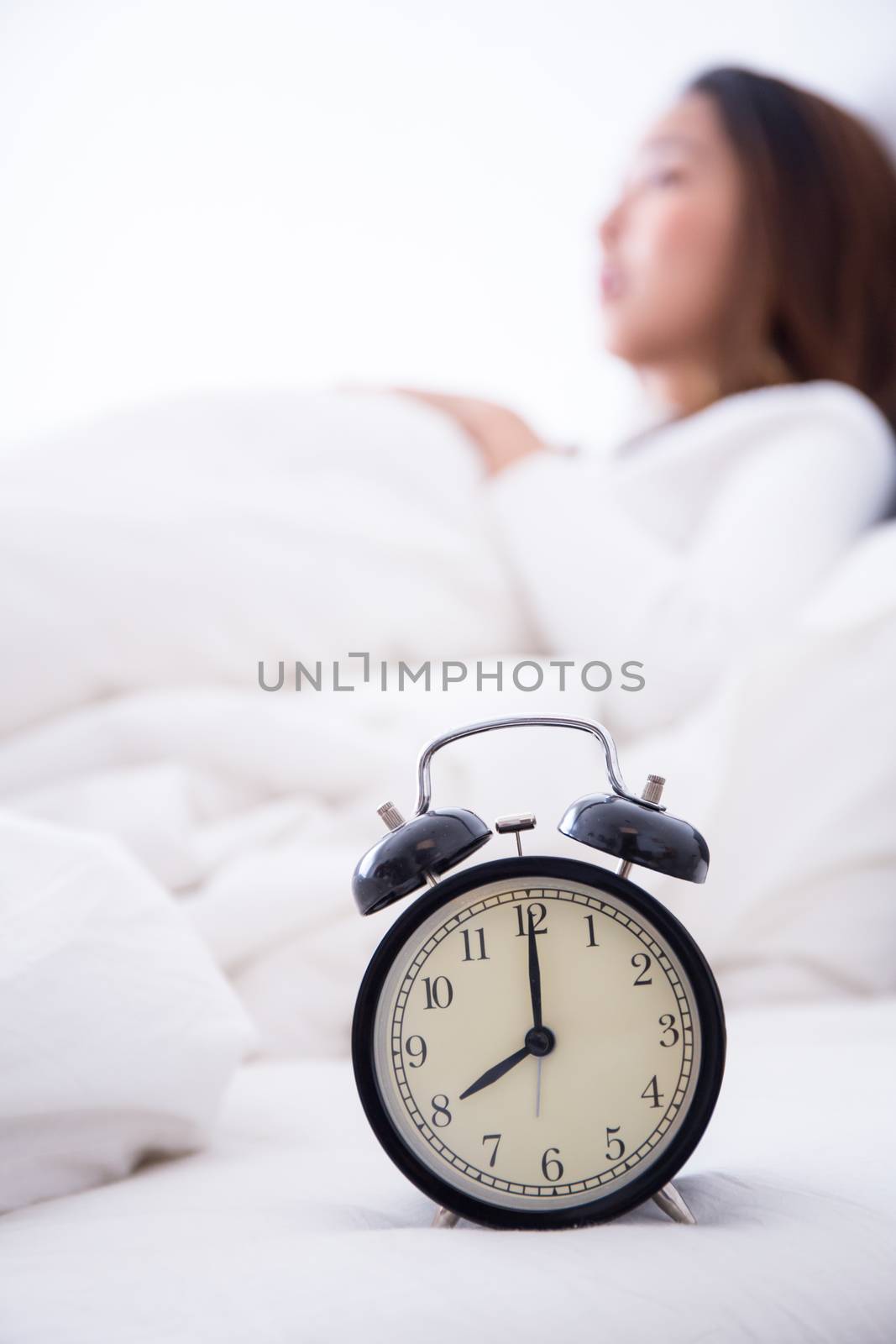 alarm clock standing on bedside table going to ring early morning to wake up woman in bed sleeping in background - early awakening -not getting enough sleep - getting work time concept