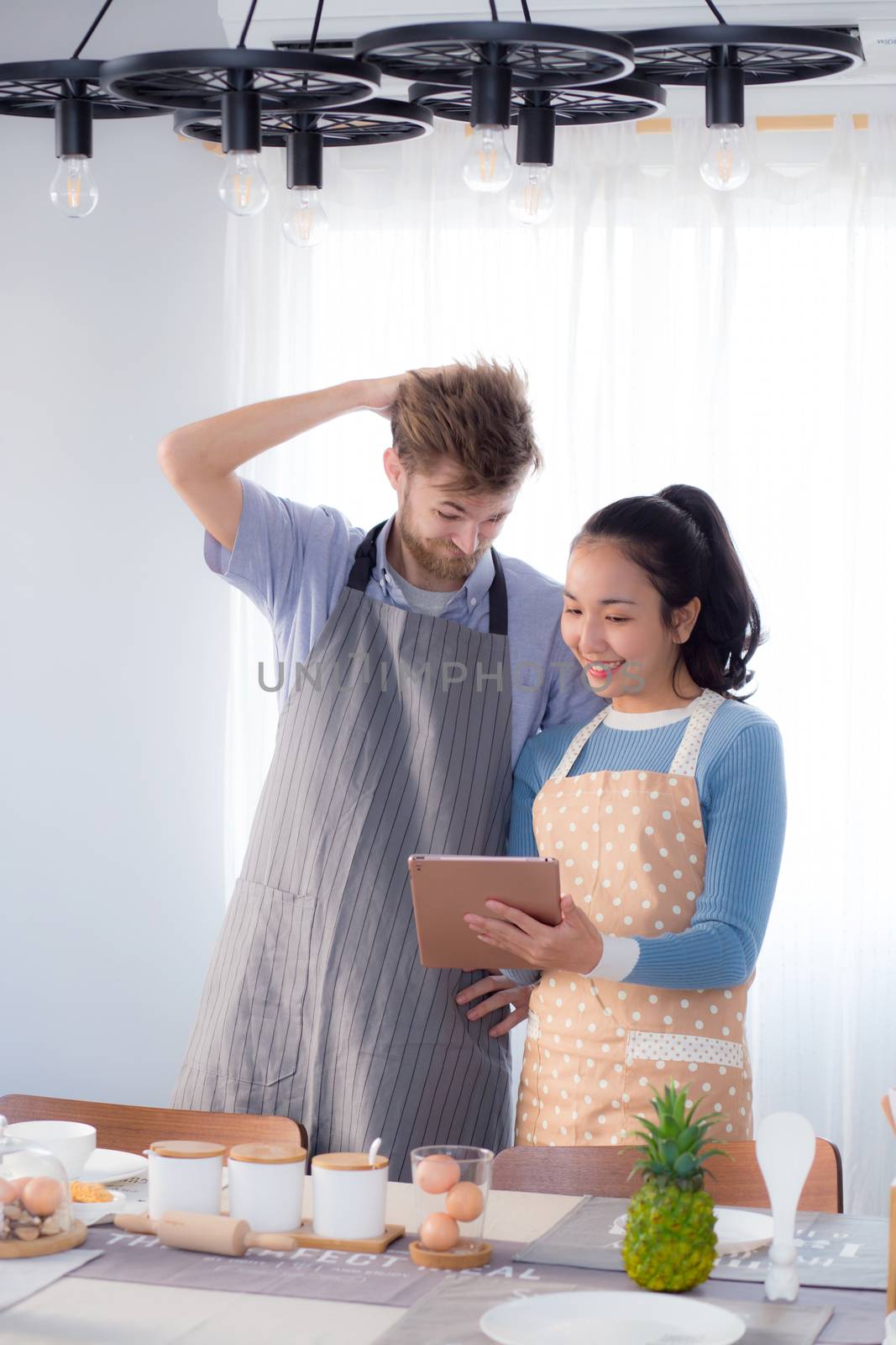 Young couple in kitchen looking at tablet - Man and girl using digital tablet in kitchen.