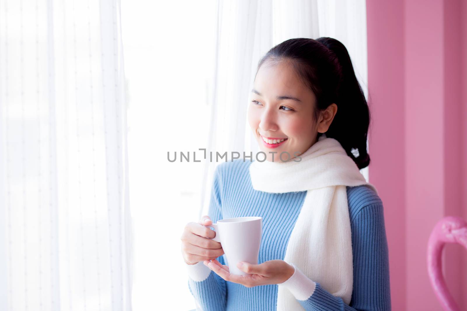 Beautiful young woman is looking out the window and holding a cup of coffee in morning.