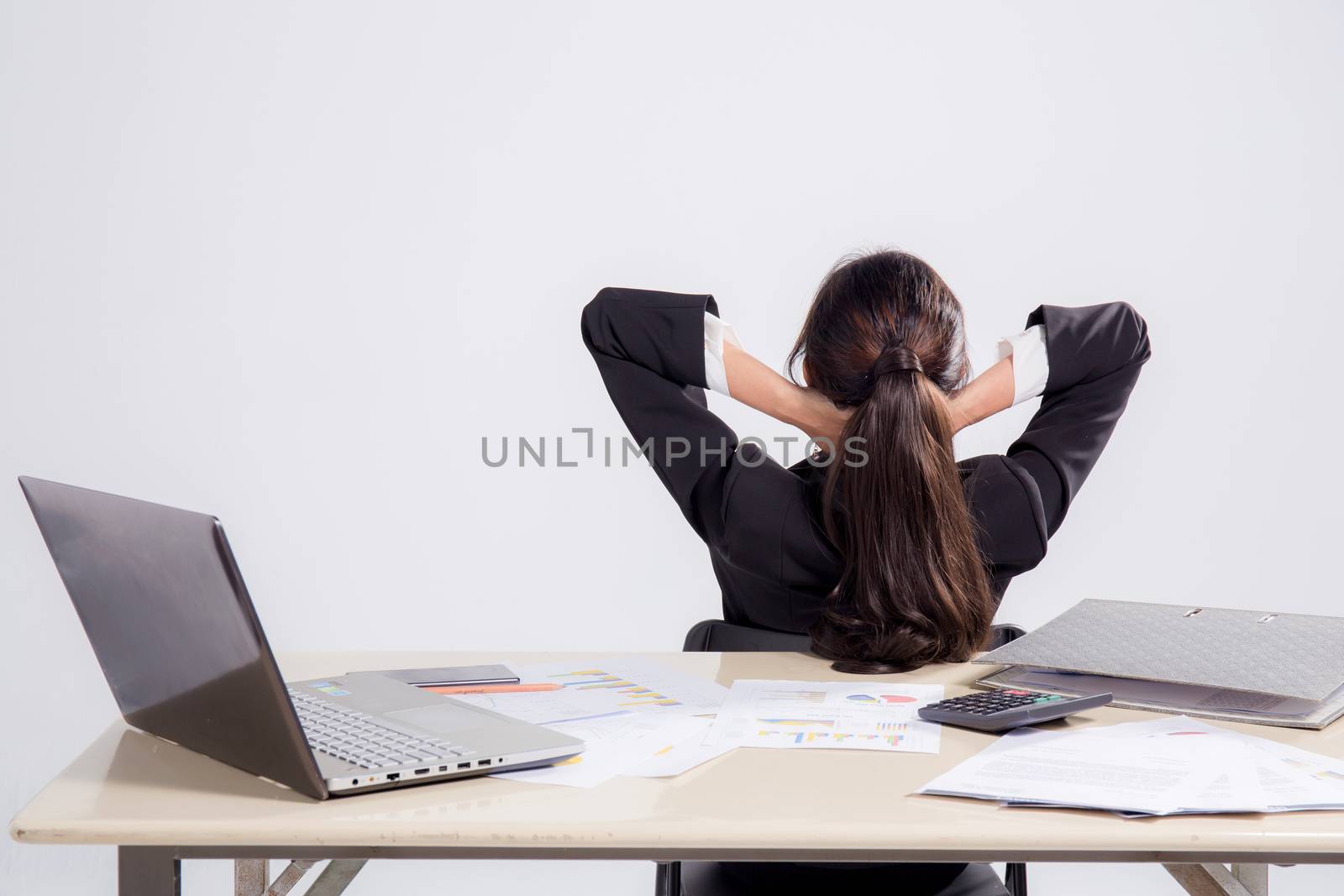 Closeup portrait of cute young relaxed business woman from behind with open hands behind her head on work space
