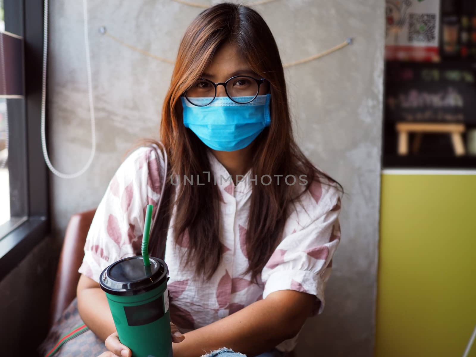 Asian woman wears a protective mask on her face while sitting in a coffee shop. New normal concept. COVID-19.