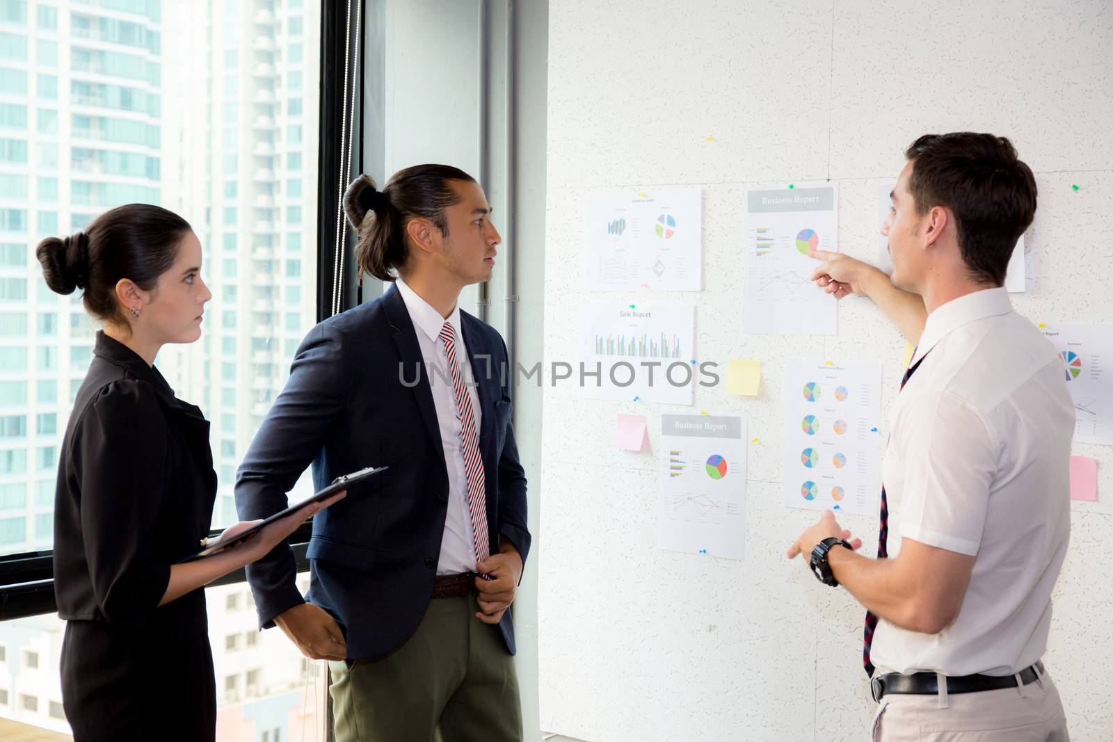 young businesspeople pointing towards graph with present profit while giving presentation in office.