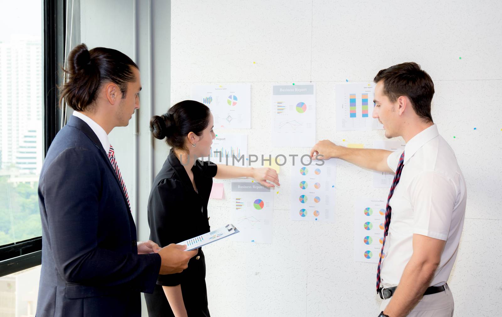 young businesspeople pointing towards graph with present profit while giving presentation in office.