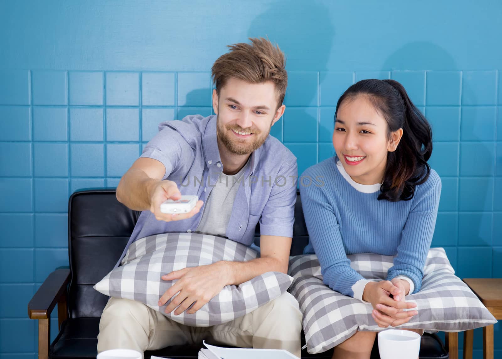 Happy young couple lying on the sofa with push remote at home watching TV.