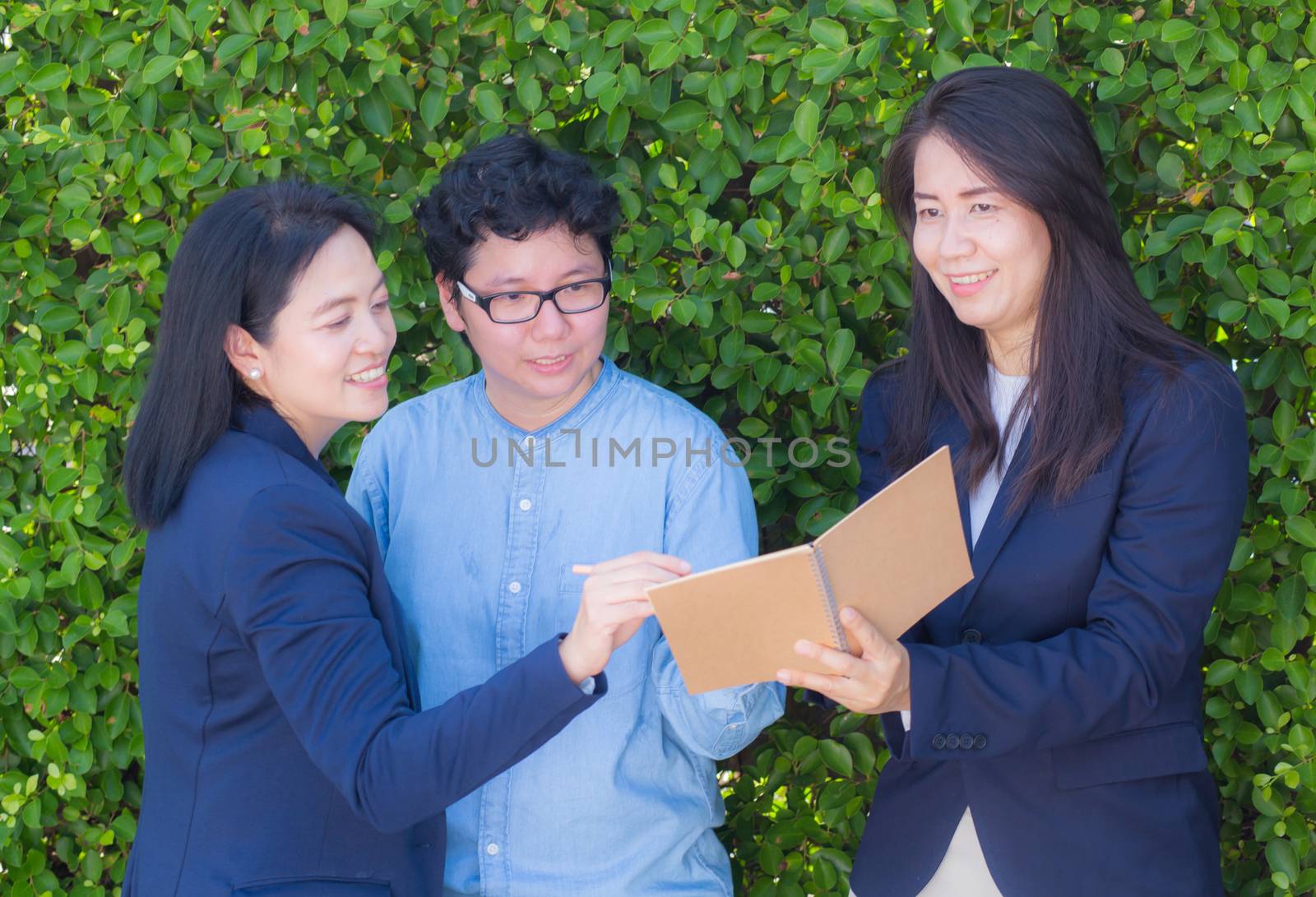 Businesswomen three people looking information on notebook or diary corporate on tree wall.