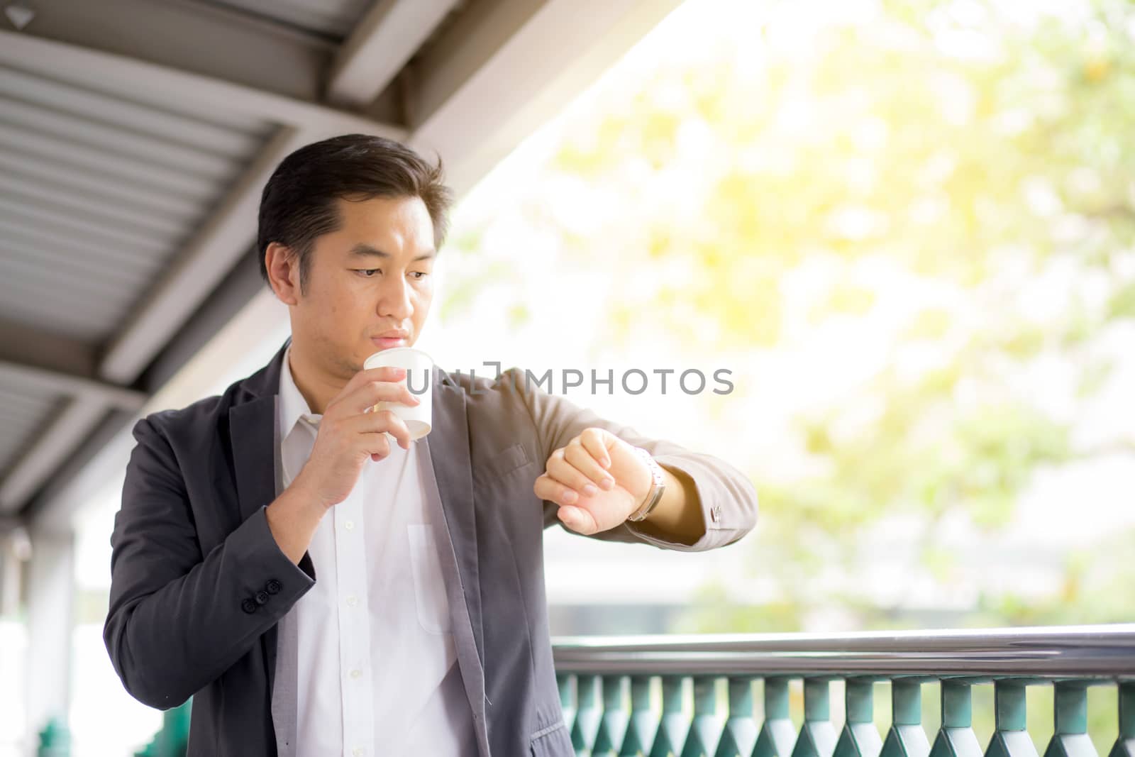 Portrait of young handsome business man drinking coffee looking at wrist watch - Waiting concept.