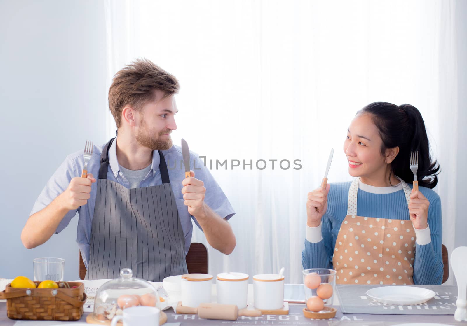 Young family couple sitting at the table in the kitchen and holding spoon and fork together.