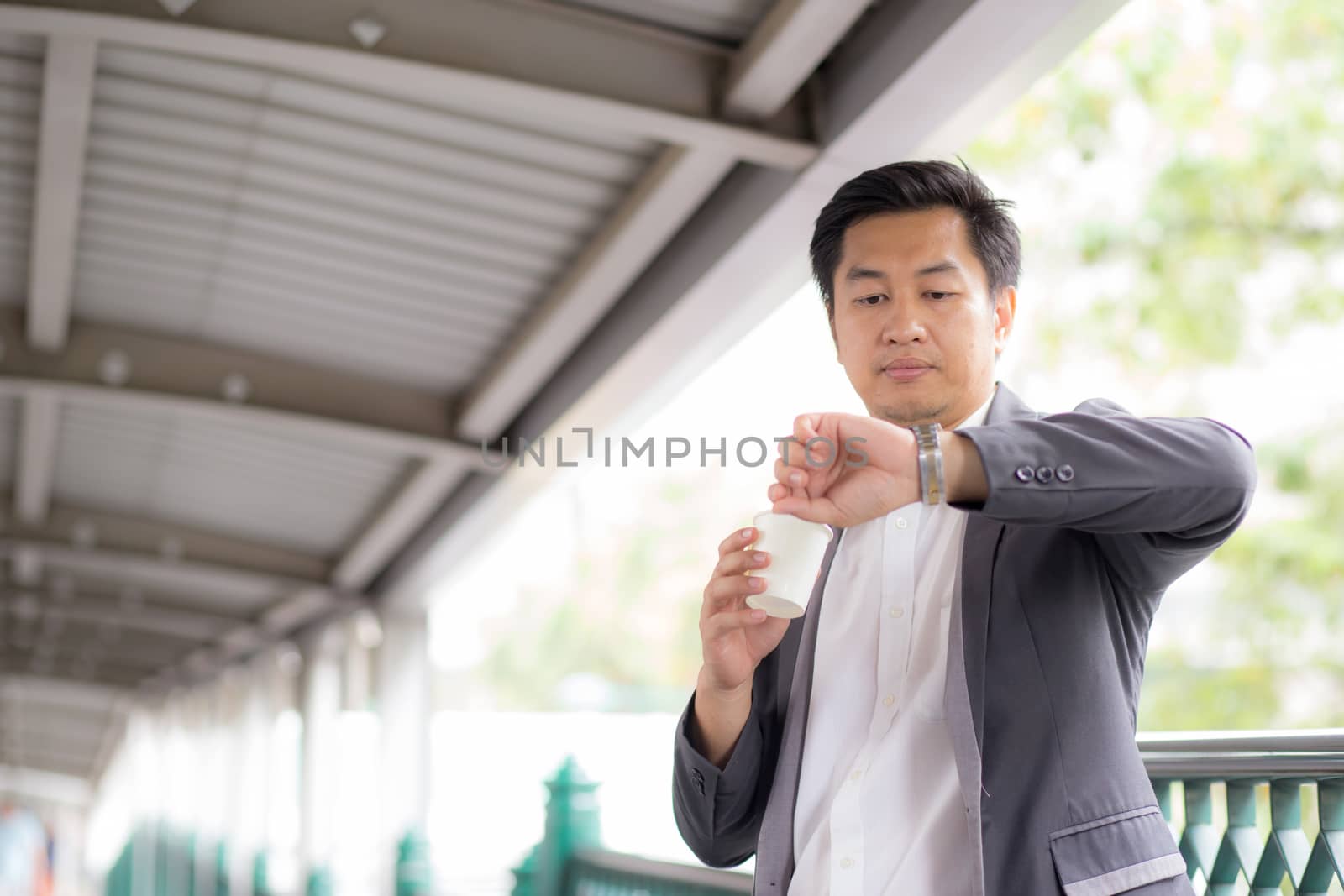 Portrait of young handsome business man drinking coffee looking at wrist watch - Waiting concept.
