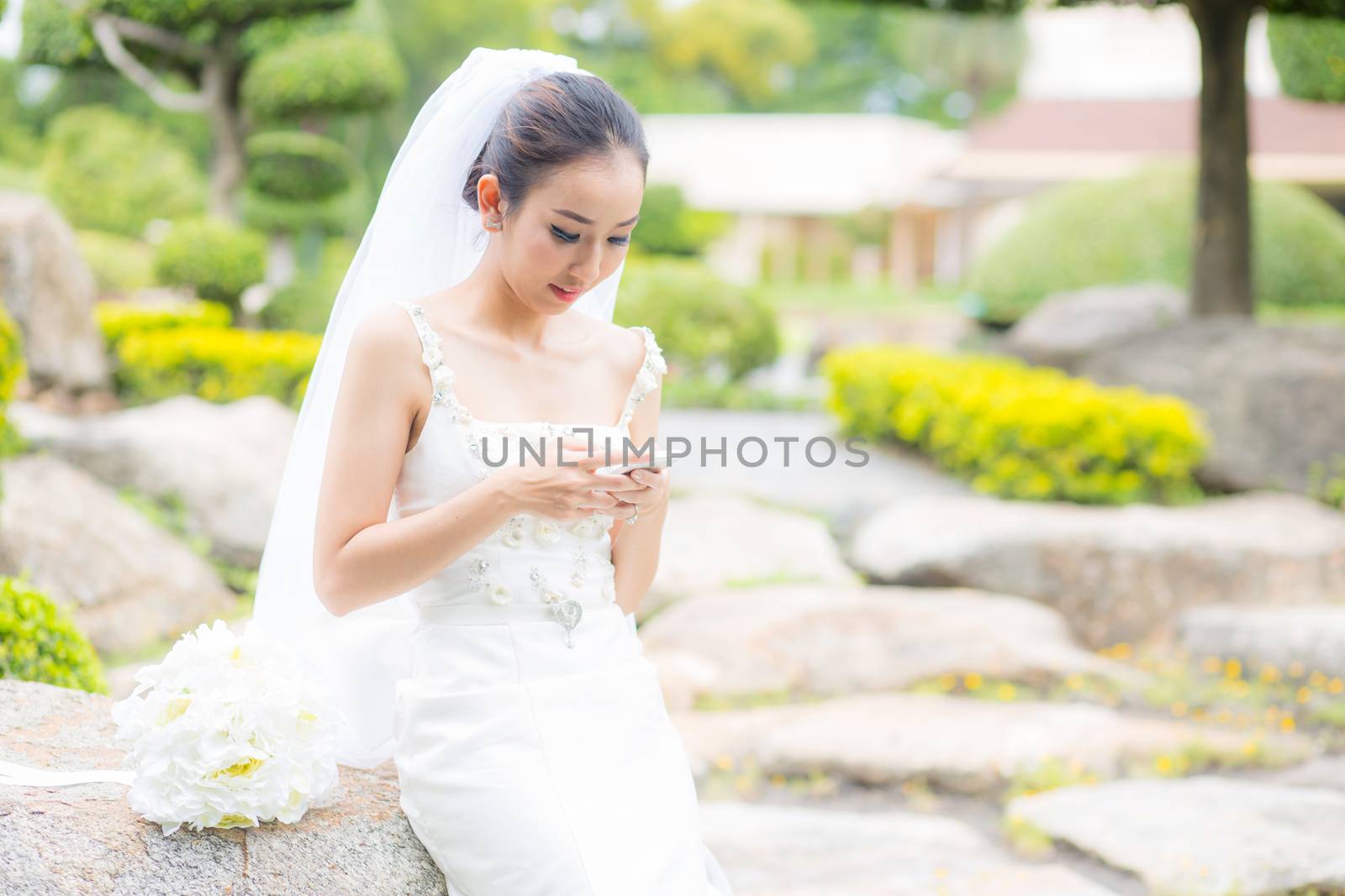 bride touch on phone in wedding dress on garden.
