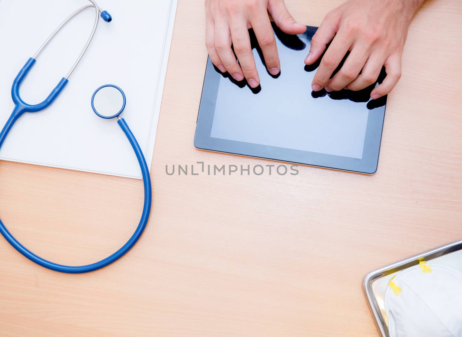 male doctor with tablet computer and stethoscope at the desk on white background - top view.
