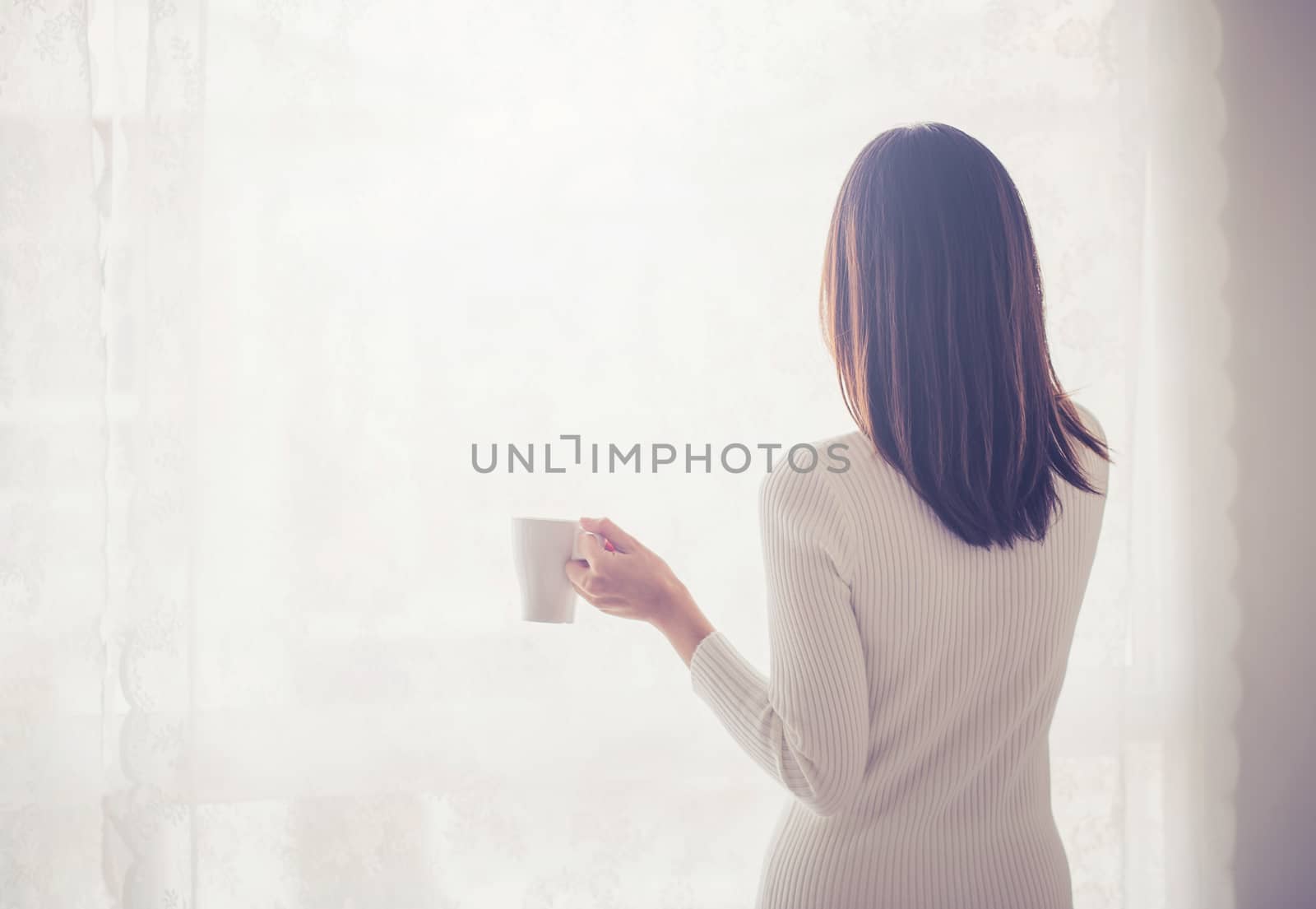Beautiful young woman asian behind holding drinking coffee at a window.