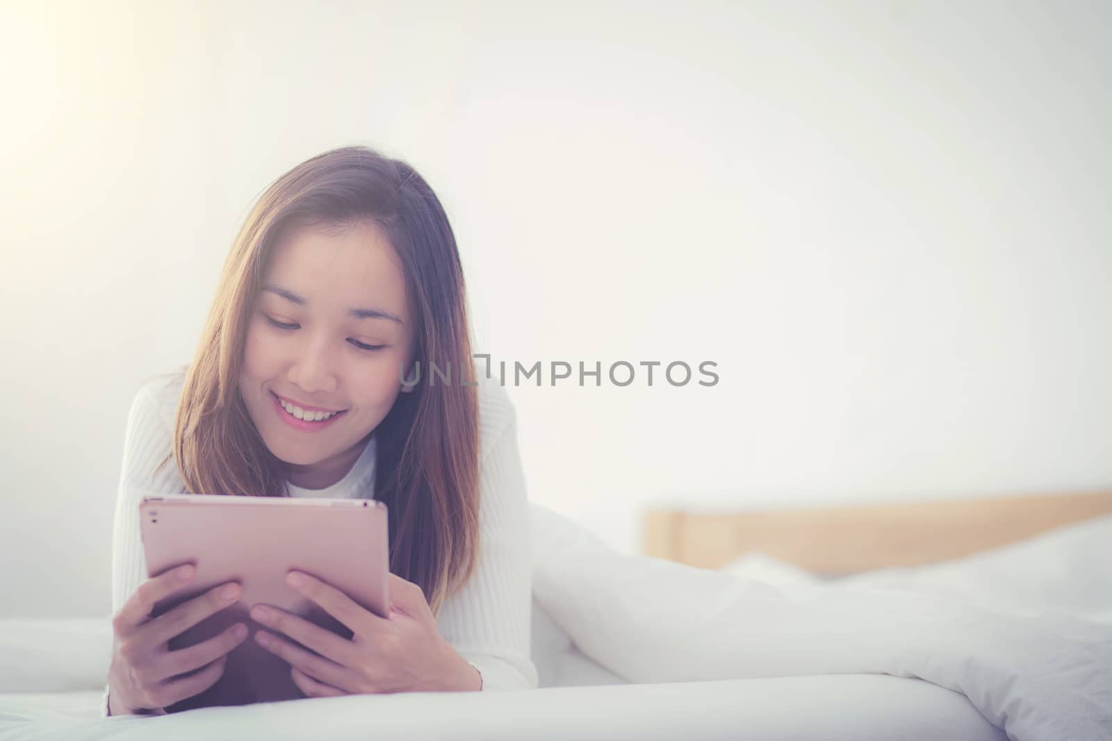 woman asian lying in bedroom with digital tablet touching with finger in morning sunlight