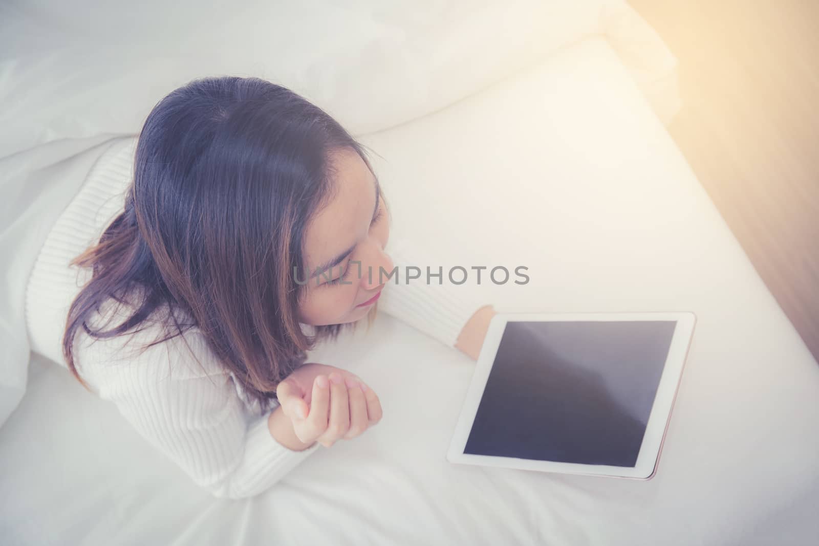 woman asian lying in bedroom with digital tablet touching with finger in morning sunlight
