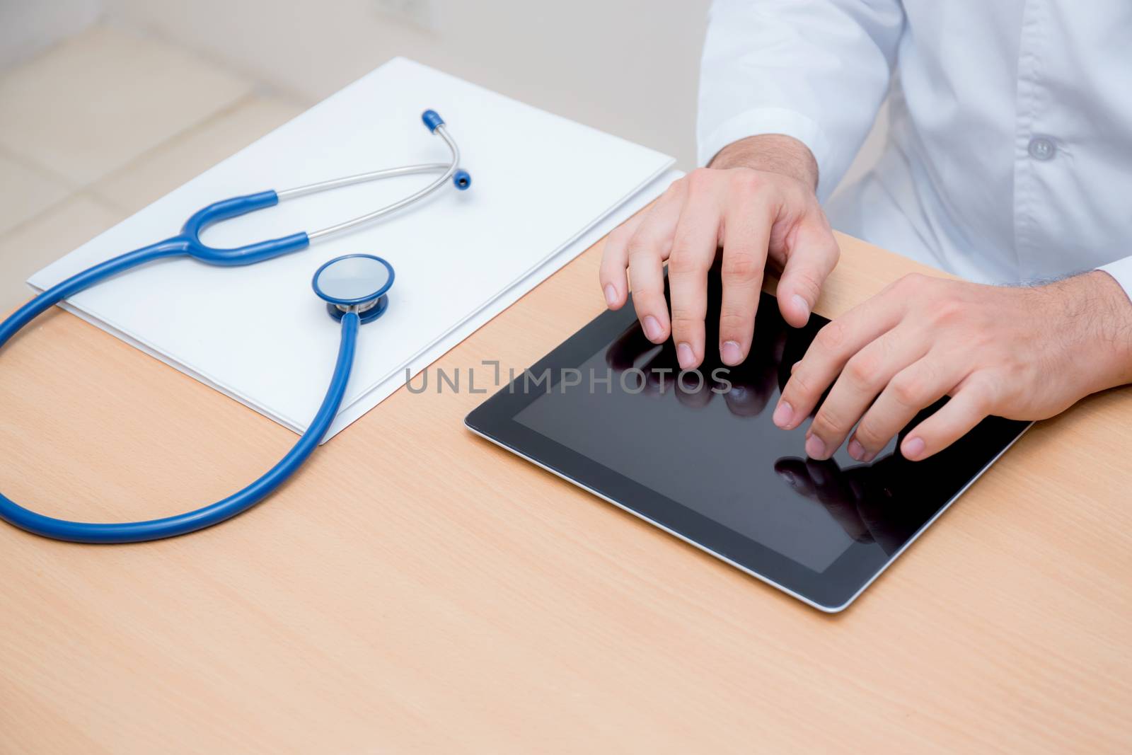 male doctor with tablet computer and stethoscope at the desk on white background.
