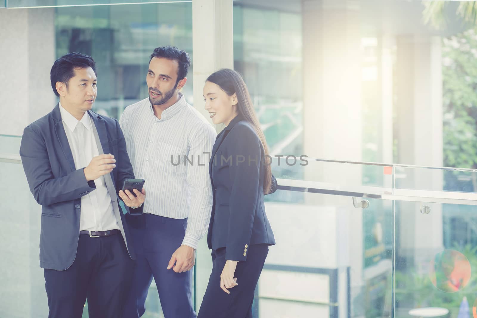 Two handsome young businessmen and lady in classic suits, talking and smiling, standing outside the office building.