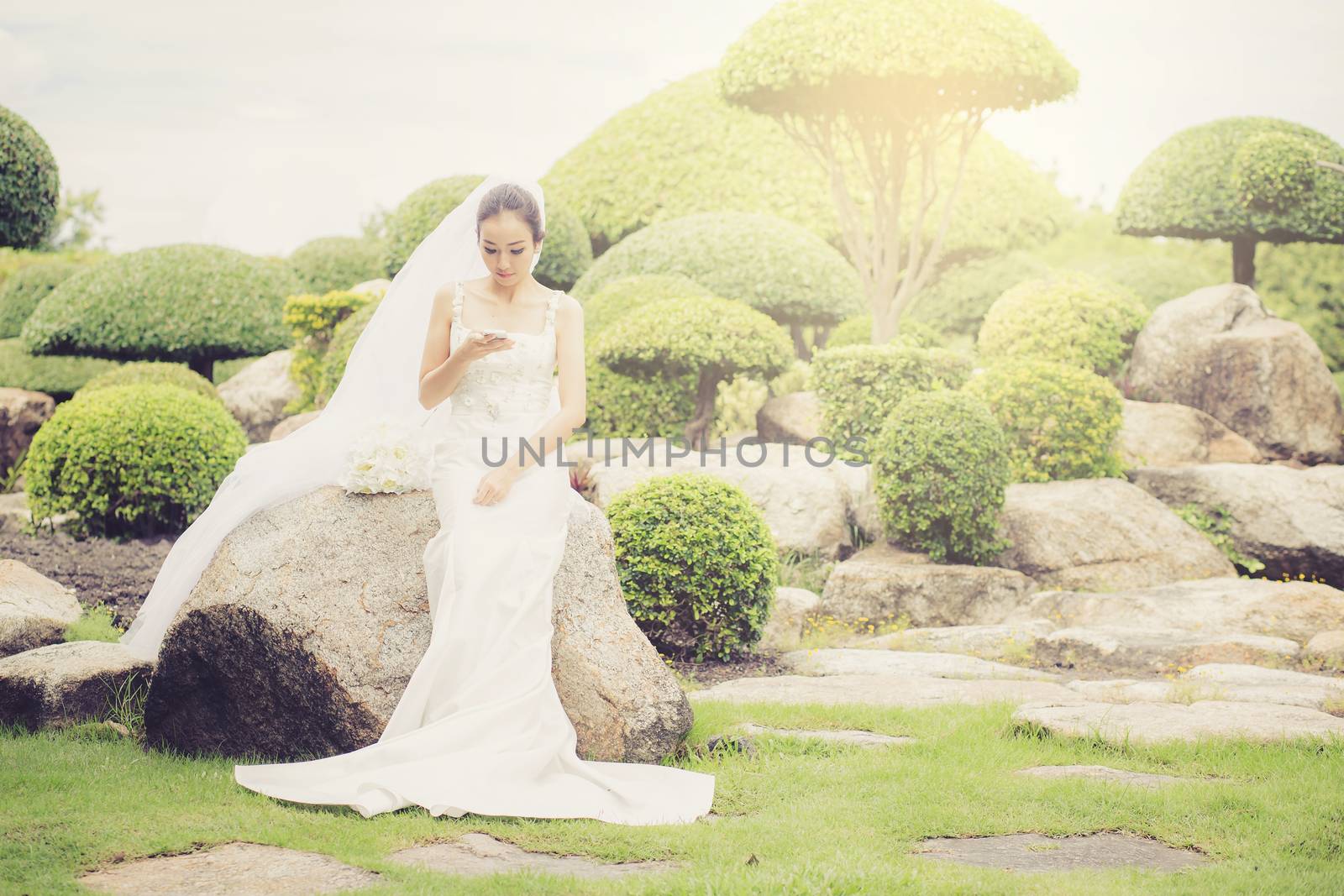 bride touch on phone in wedding dress on garden. by nnudoo