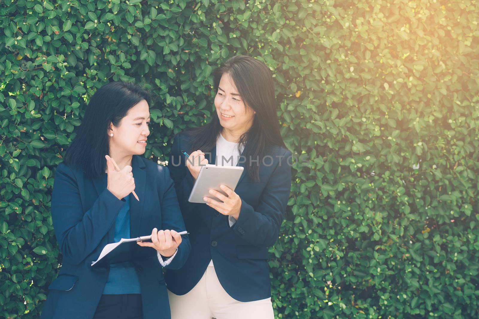 Two business people discussing information on a tablet-and taking notes as they work together as a team in the garden.