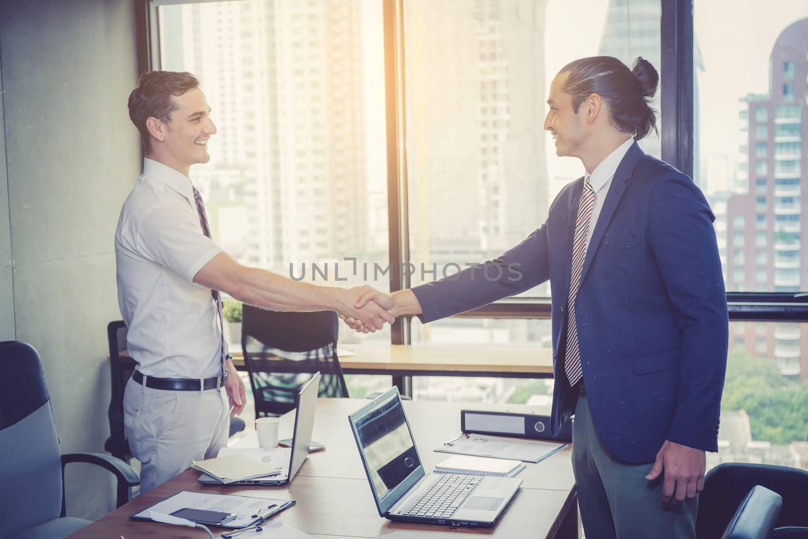 Two happy successful business partner shaking hands in the office.