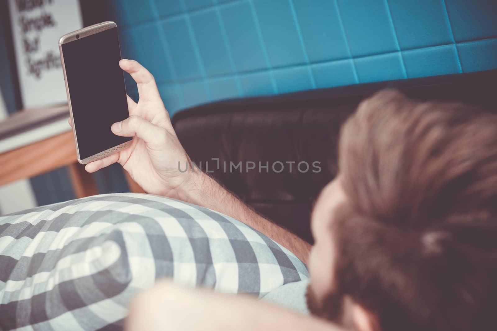Happy man watching media content in a smart phone sitting on a couch at home, Top side view mock up background