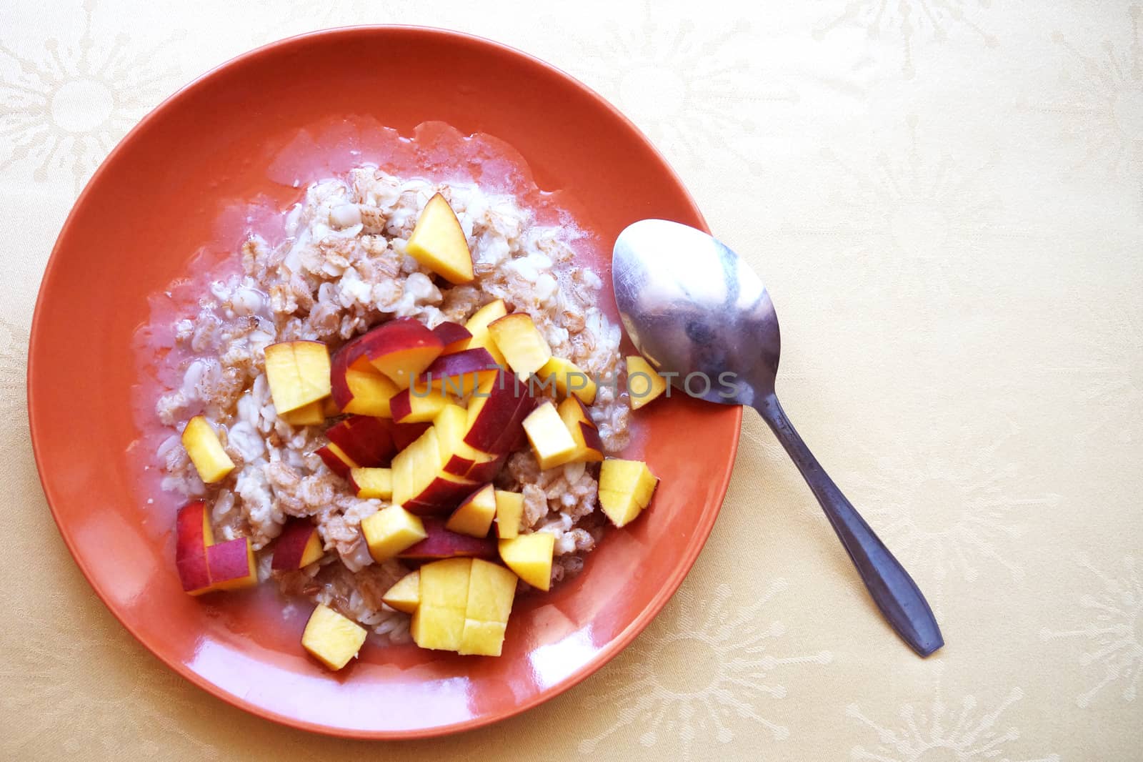 oatmeal porridge with chopped fresh peach in a plate with a spoon, vegetarian breakfast. by Annado