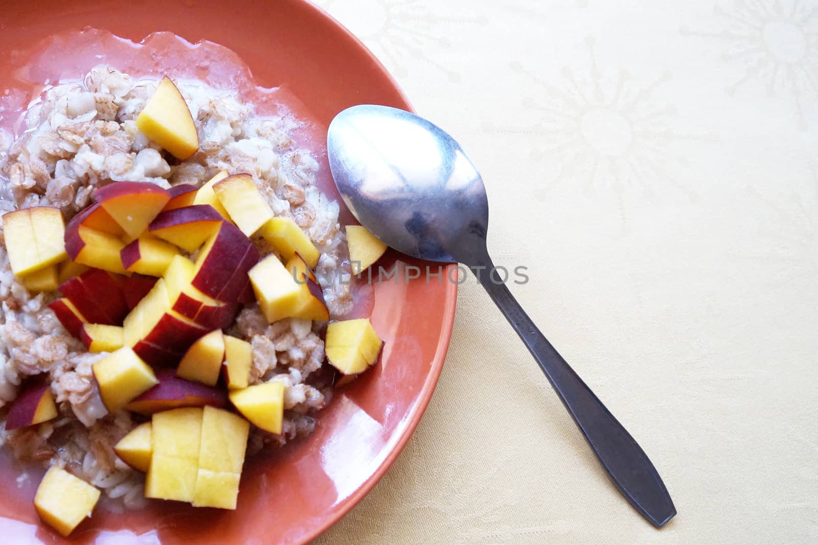 oatmeal porridge with chopped fresh peach in a plate with a spoon, vegetarian breakfast.