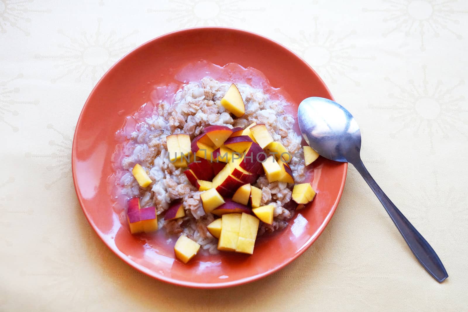 oatmeal porridge with chopped fresh peach in a plate with a spoon, vegetarian breakfast. by Annado