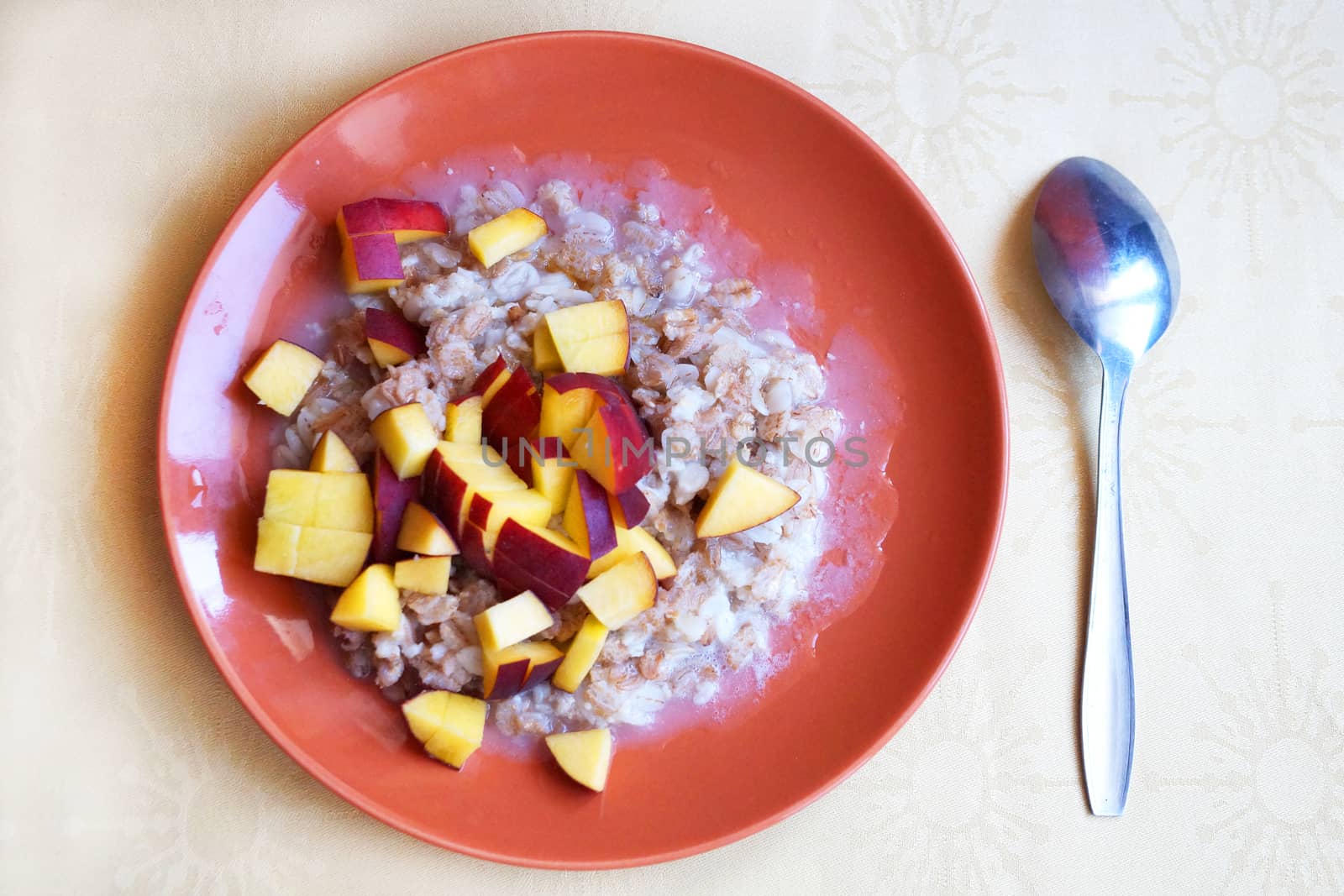 oatmeal porridge with chopped fresh peach in a plate with a spoon, vegetarian breakfast.