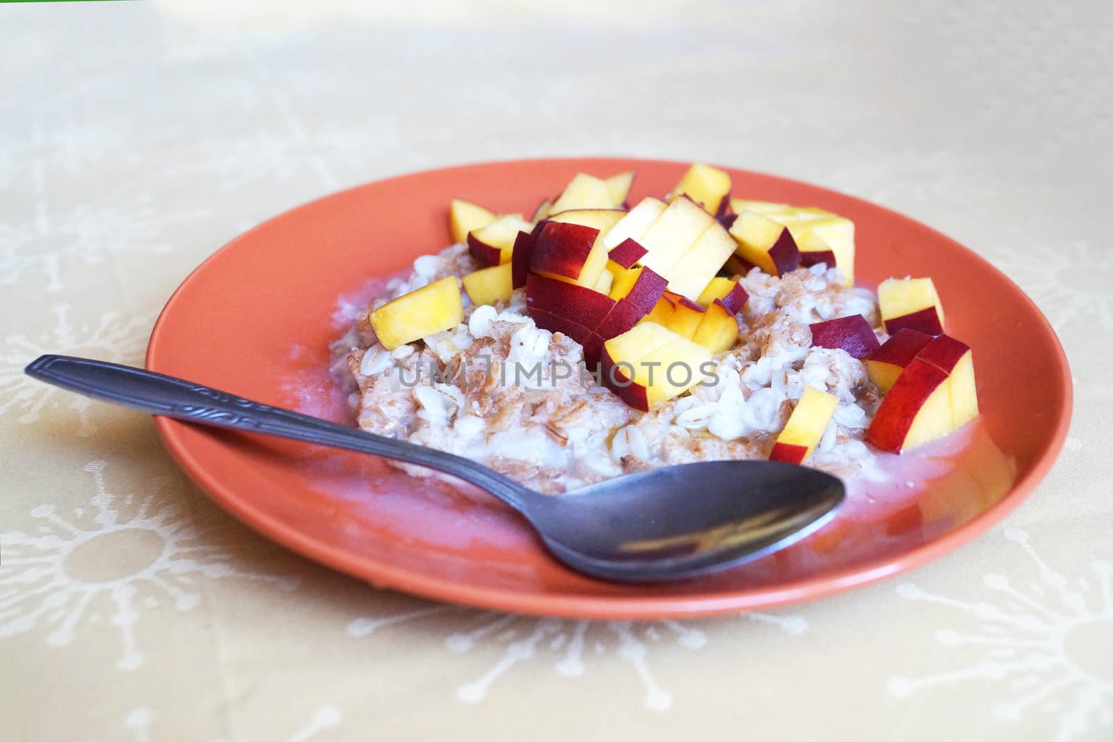 oatmeal porridge with chopped fresh peach in a plate with a spoon, vegetarian breakfast. by Annado