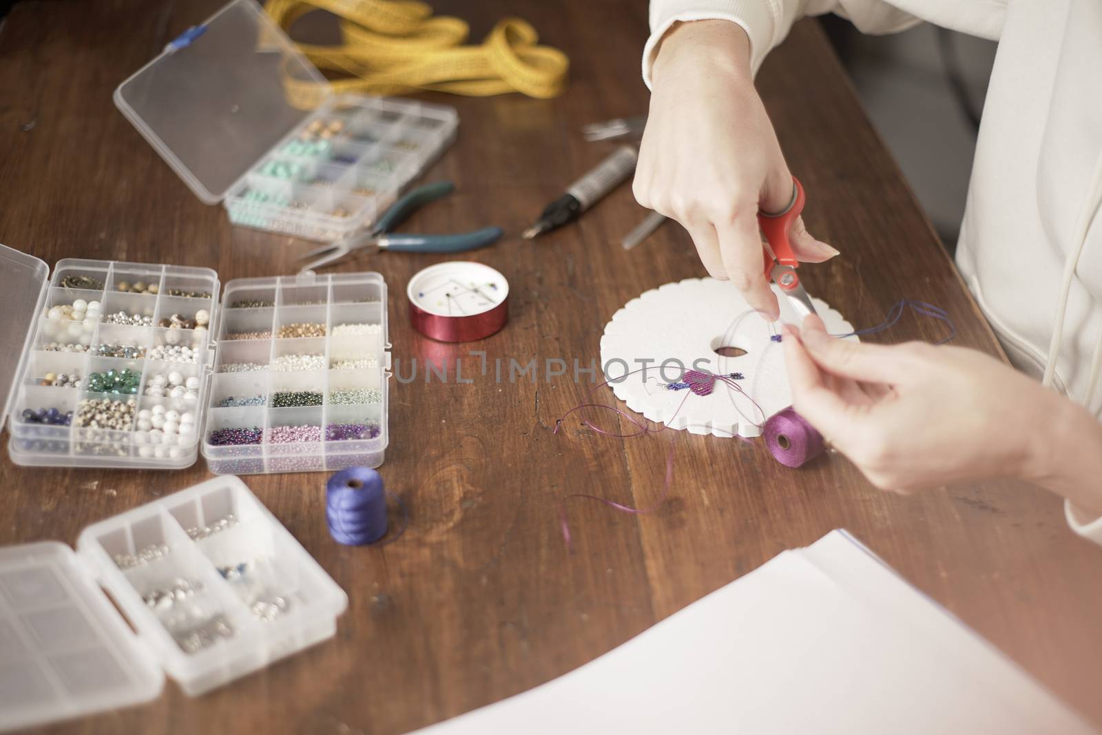 Lifestyle concept, work from home to reinvent your life: close-up of woman hands making macrame woman cuts the wire with the appropriate tool to finish the job on kumihimo tools on wooden table by robbyfontanesi