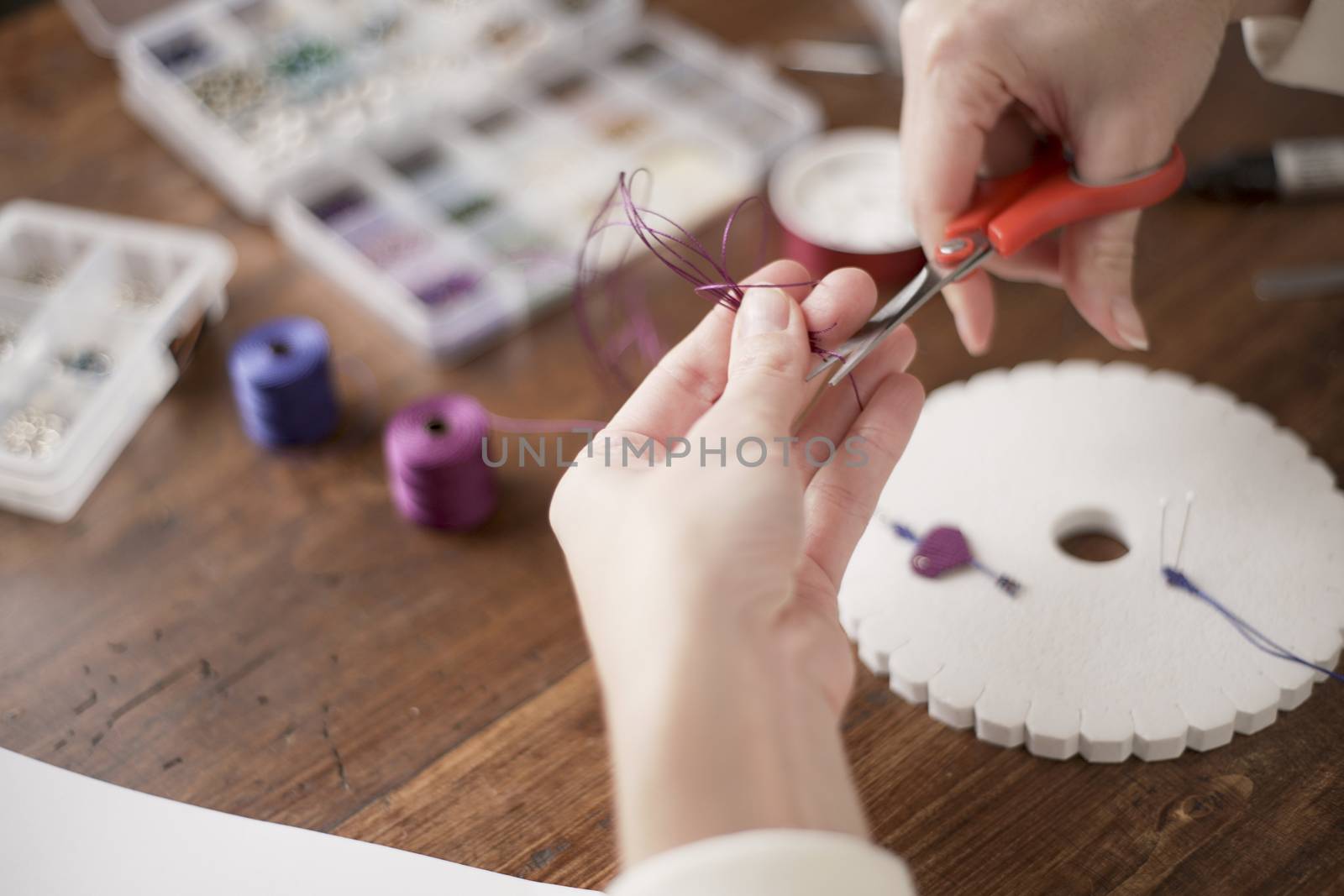 Lifestyle concept, work from home to reinvent your life: close-up of woman hands making macrame knots the fuchsia thread creating an earring on kumihimo tools on wooden table by robbyfontanesi