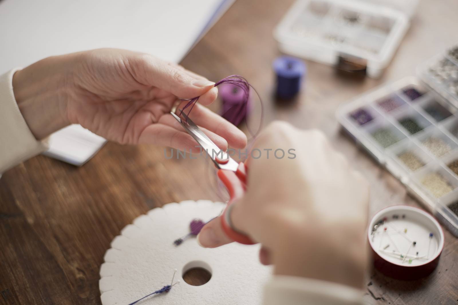 Lifestyle concept, work from home to reinvent your life: close-up of woman hands making macrame knots the fuchsia thread creating an earring on kumihimo tools on wooden table by robbyfontanesi