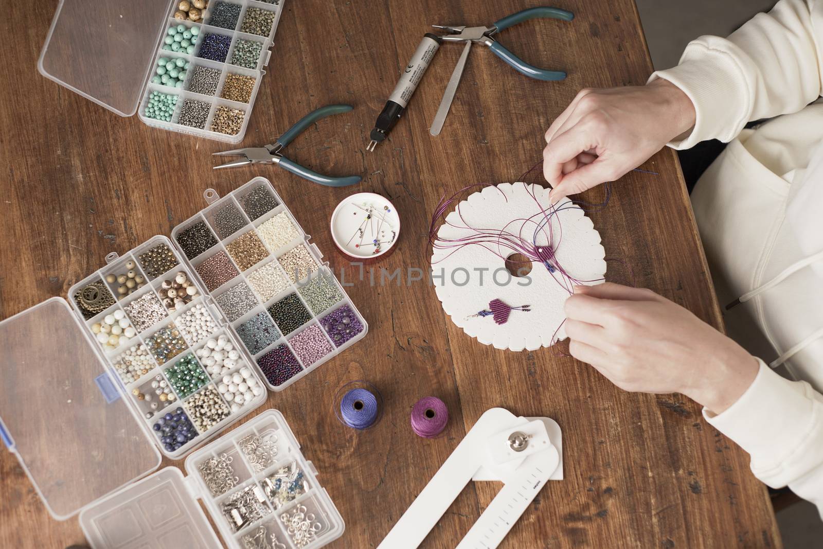 Lifestyle concept, work from home to reinvent your life: top view of woman hands making macrame knots the fuchsia thread creating an earring on kumihimo tools on wooden table by robbyfontanesi