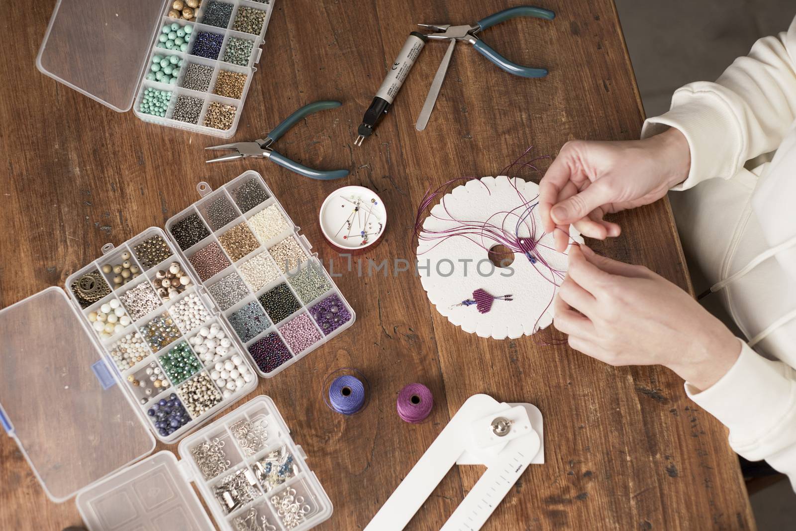 Lifestyle concept, work from home to reinvent your life: close-up of woman hands making macrame knots the fuchsia thread creating an earring on kumihimo tools on wooden table