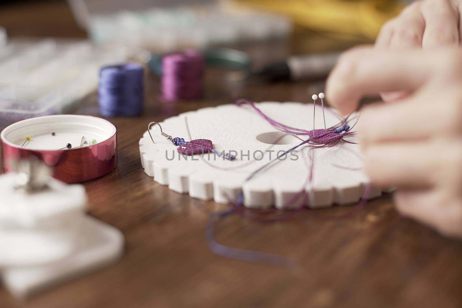 Lifestyle concept, work from home to reinvent your life: close-up of woman hands making macrame knots the fuchsia thread creating an earring on kumihimo tools on wooden table by robbyfontanesi