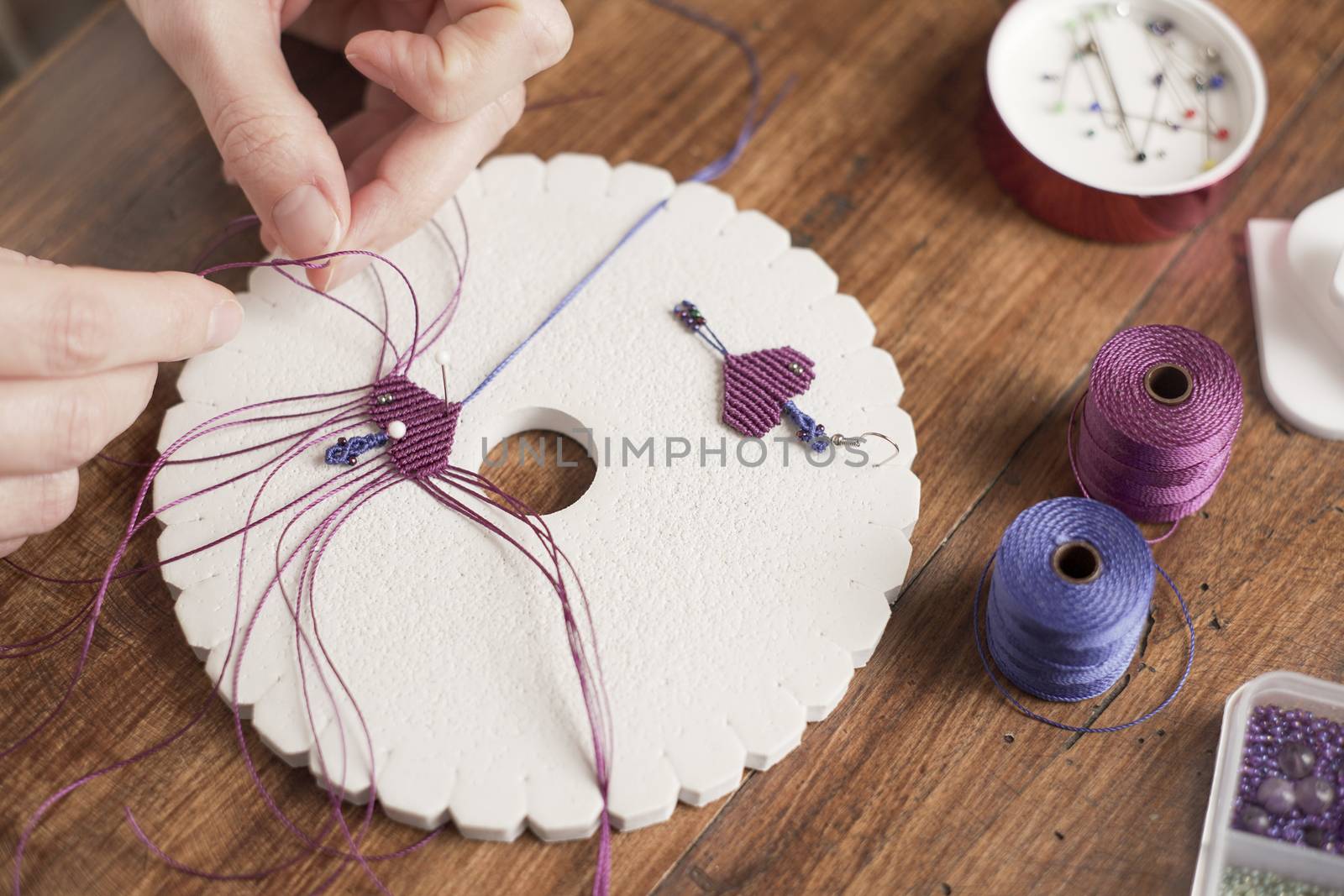 Lifestyle concept, work from home to reinvent your life: close-up of woman hands making macrame knots the fuchsia thread creating an earring on kumihimo tools on wooden table