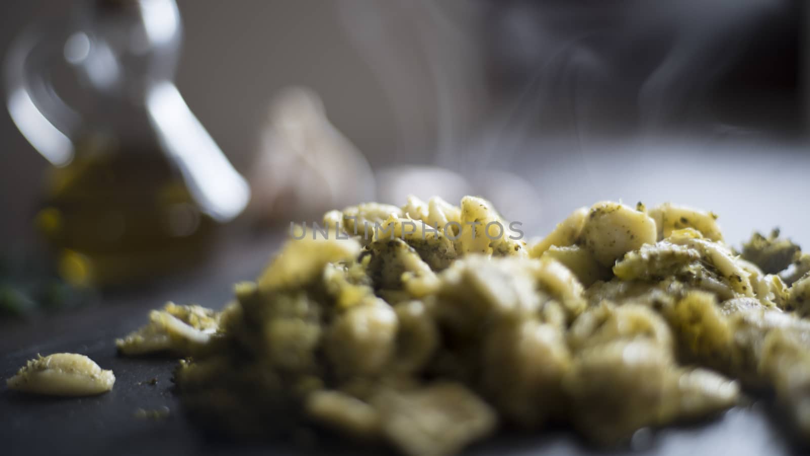 Closeup of a slate plate with steaming orecchiette with broccoli, typical Apulian recipe, in backlight on dark wooden table with olive oil and garlic on background in bokeh effect