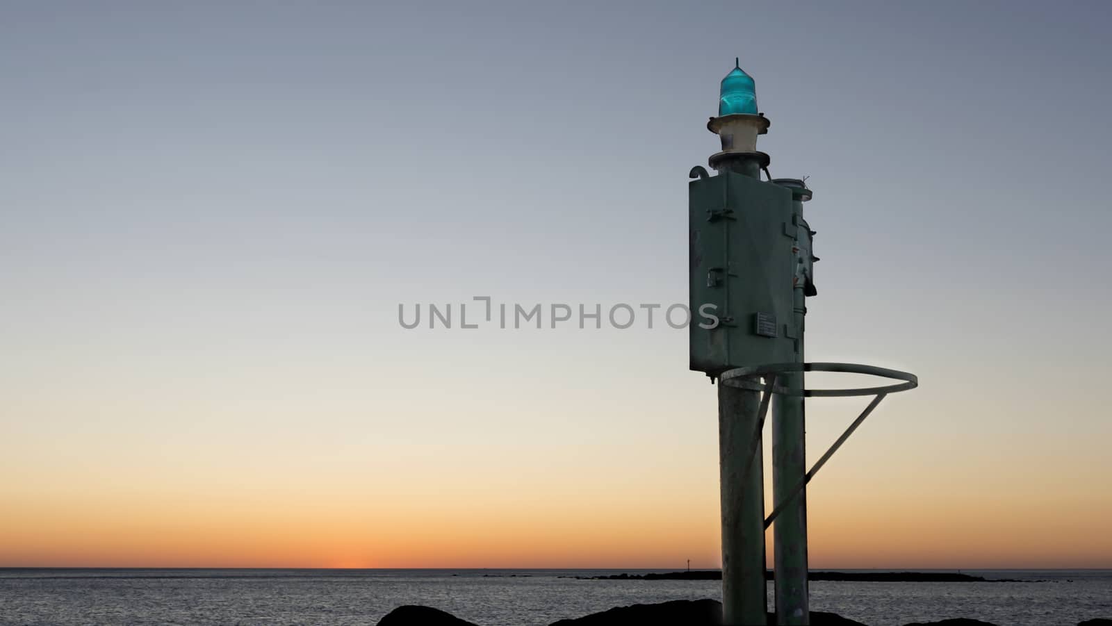 The sea at dawn or sunset with a small lighthouse in the harbor in the foreground