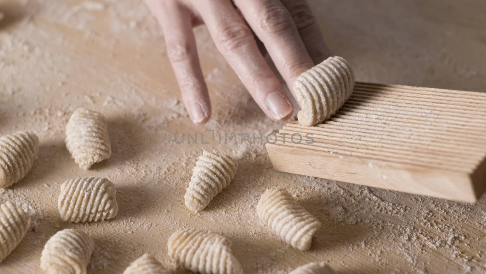 Close up process of homemade vegan gnocchi pasta with wholemeal flour making. The home cook crawls on the special wooden tool the gnocco , traditional Italian pasta, woman cooks food in the kitchen