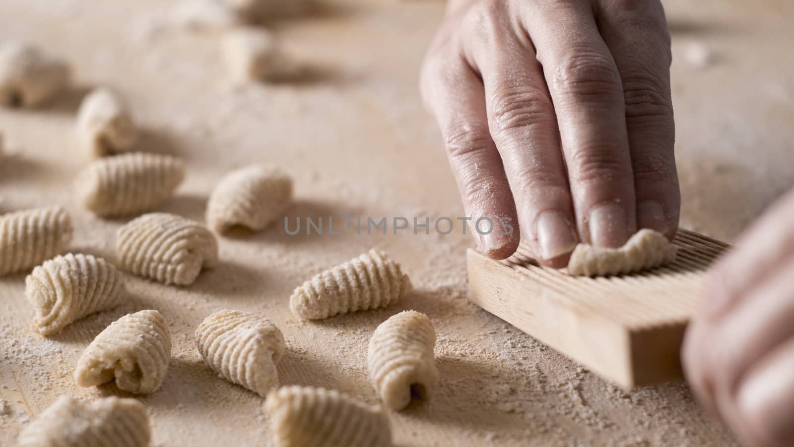 Close up process of homemade vegan gnocchi pasta with wholemeal flour making. The home cook crawls on the special wooden tool the gnocco , traditional Italian pasta, woman cooks food in the kitchen by robbyfontanesi