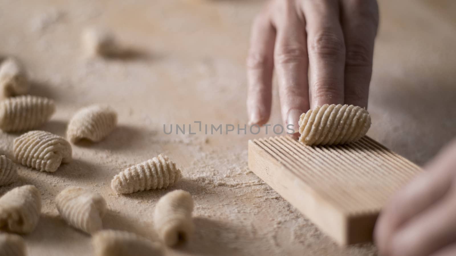 Close up process of homemade vegan gnocchi pasta with wholemeal flour making. The home cook crawls on the special wooden tool the gnocco , traditional Italian pasta, woman cooks food in the kitchen