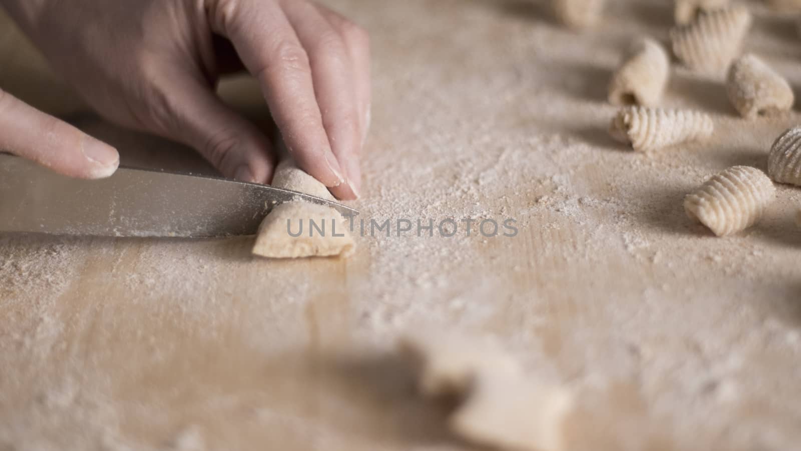 Close up process of homemade vegan gnocchi pasta with wholemeal flour making. The home cook cuts the dough on the wooden chopping board , traditional Italian pasta, woman cooks food in the kitchen by robbyfontanesi