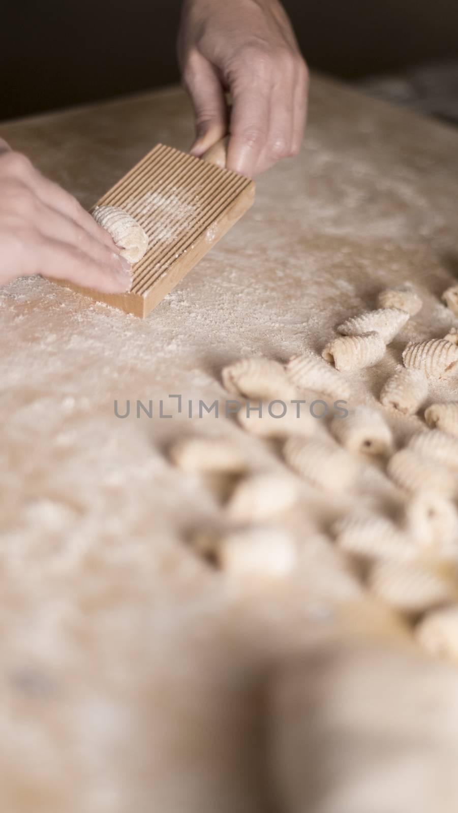 Close up process of homemade vegan gnocchi pasta with wholemeal flour making. The home cook crawls on the special wooden tool the gnocco , traditional Italian pasta, woman cooks food in the kitchen by robbyfontanesi