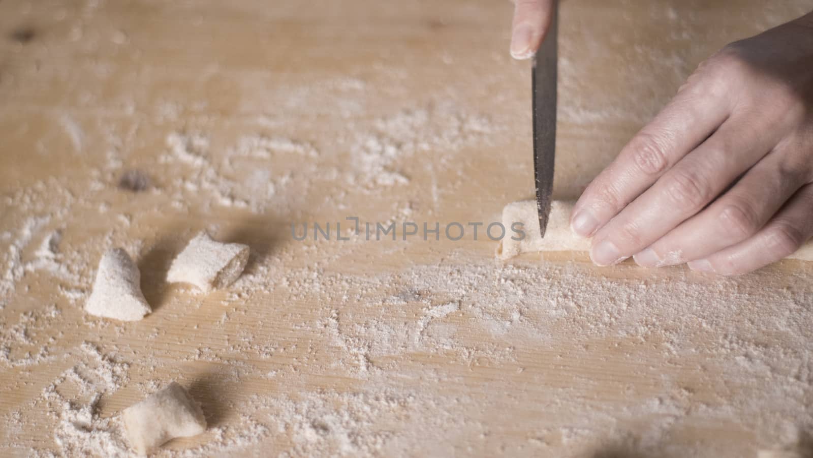 Close up process of homemade vegan gnocchi pasta with wholemeal flour making. The home cook cuts the dough on the wooden chopping board , traditional Italian pasta, woman cooks food in the kitchen by robbyfontanesi