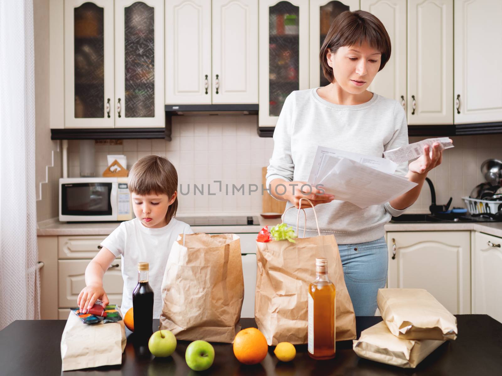 Woman and toddler boys sorts out purchases in the kitchen. Groce by aksenovko