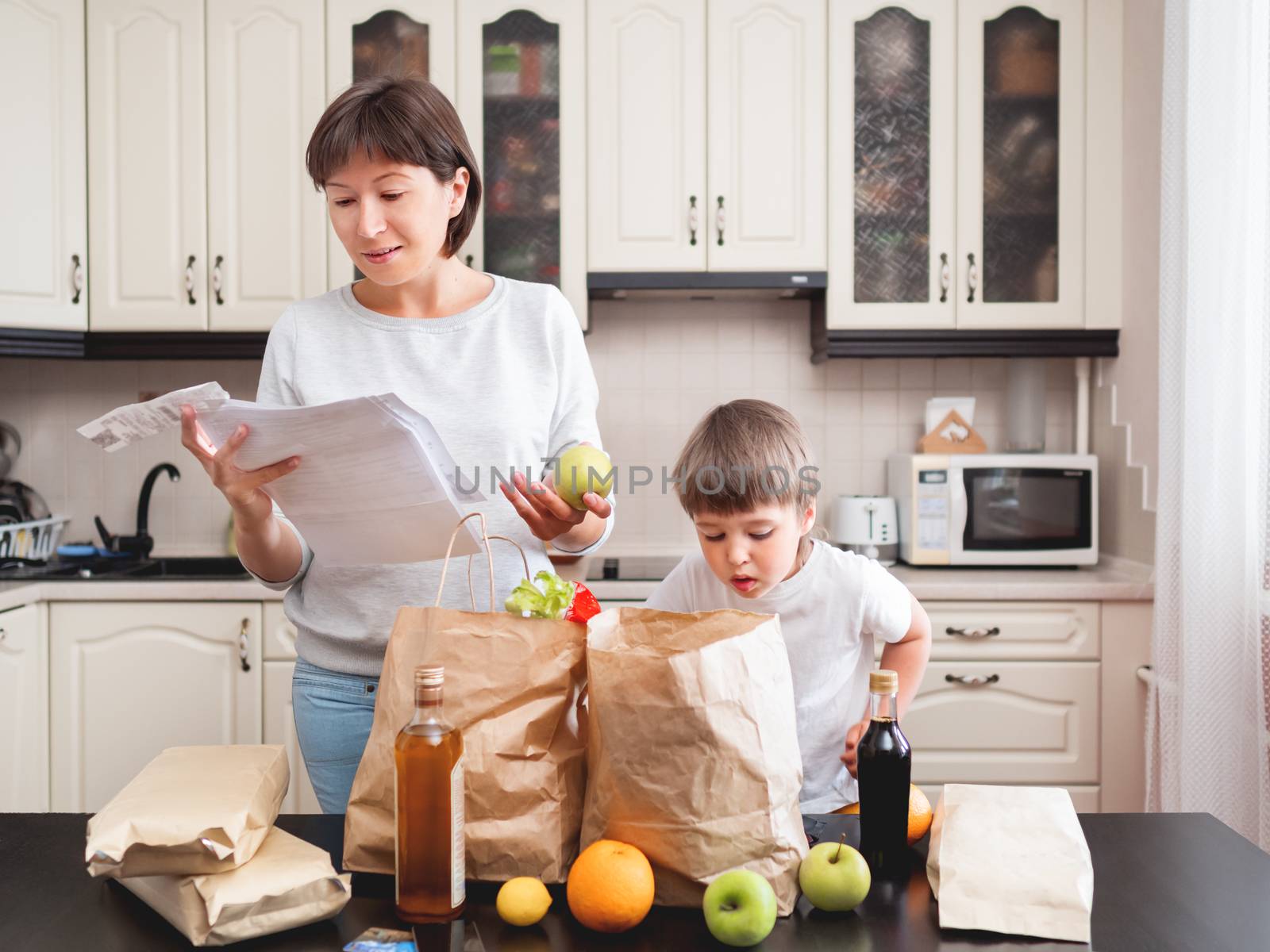 Woman and toddler boys sorts out purchases in the kitchen. Groce by aksenovko