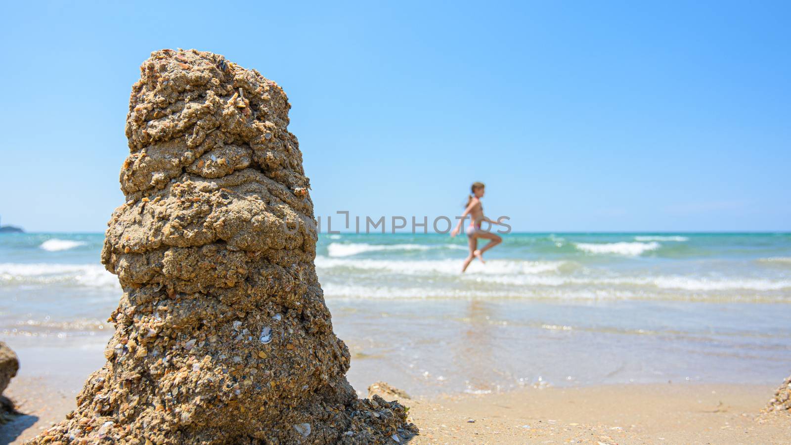 A pile of wet sand on the seashore, on the right there is an empty place for inscription, in the background a girl runs by Madhourse